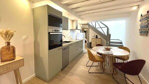 A modern kitchen with built-in appliances, a dining area with a round table and chairs, and a staircase leading to an upper level.