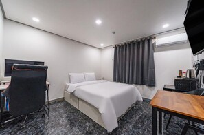 A hotel room with a bed, a desk with a chair, a table, and an air conditioning unit.