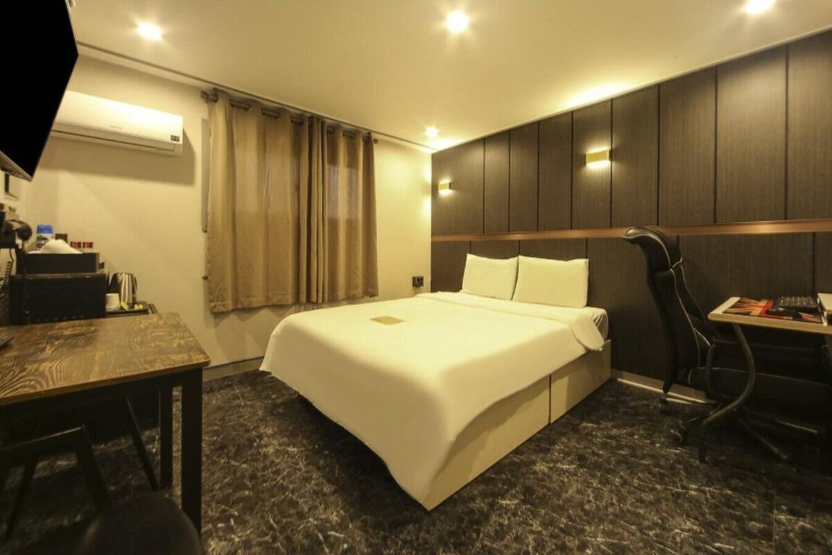 Habitación de hotel con cama, escritorio, silla, televisor y aire acondicionado.