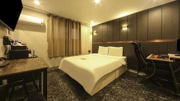 A hotel room with a bed, a desk, a chair, a TV, and an air conditioning unit.