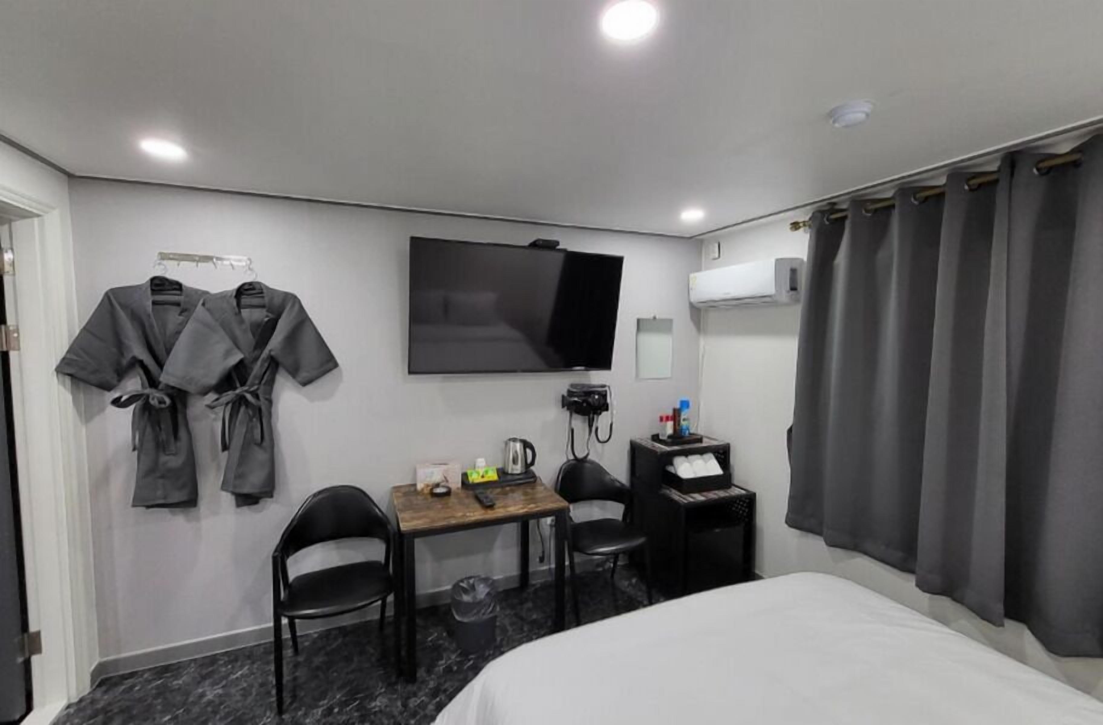 A hotel room with a bed, a desk with a chair, a TV mounted on the wall, and a robe rack.