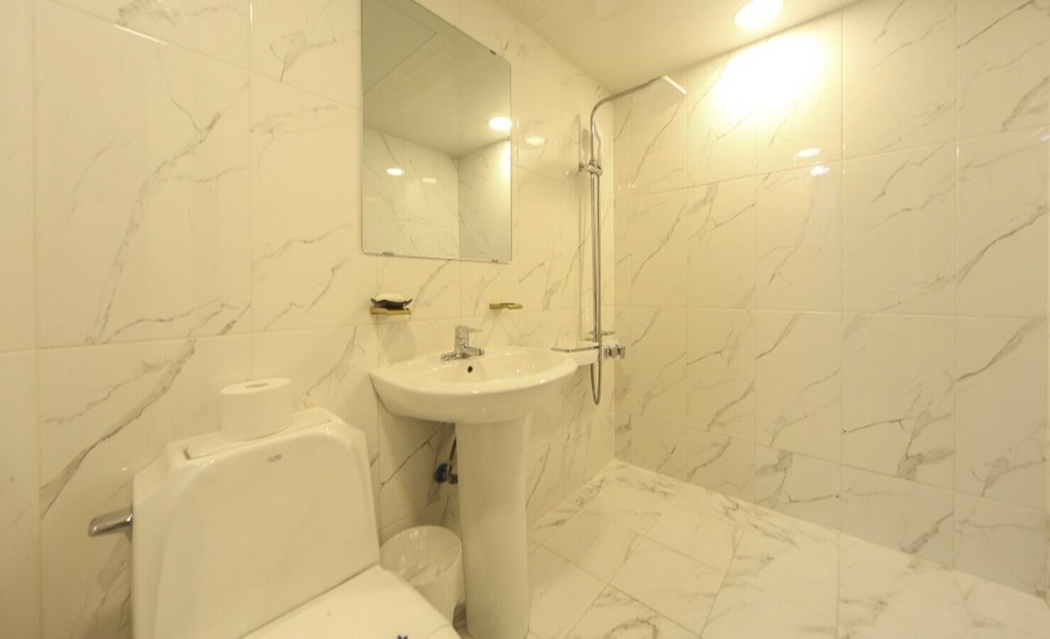 Une salle de bain avec un mur en marbre, un lavabo, des toilettes et une douche.