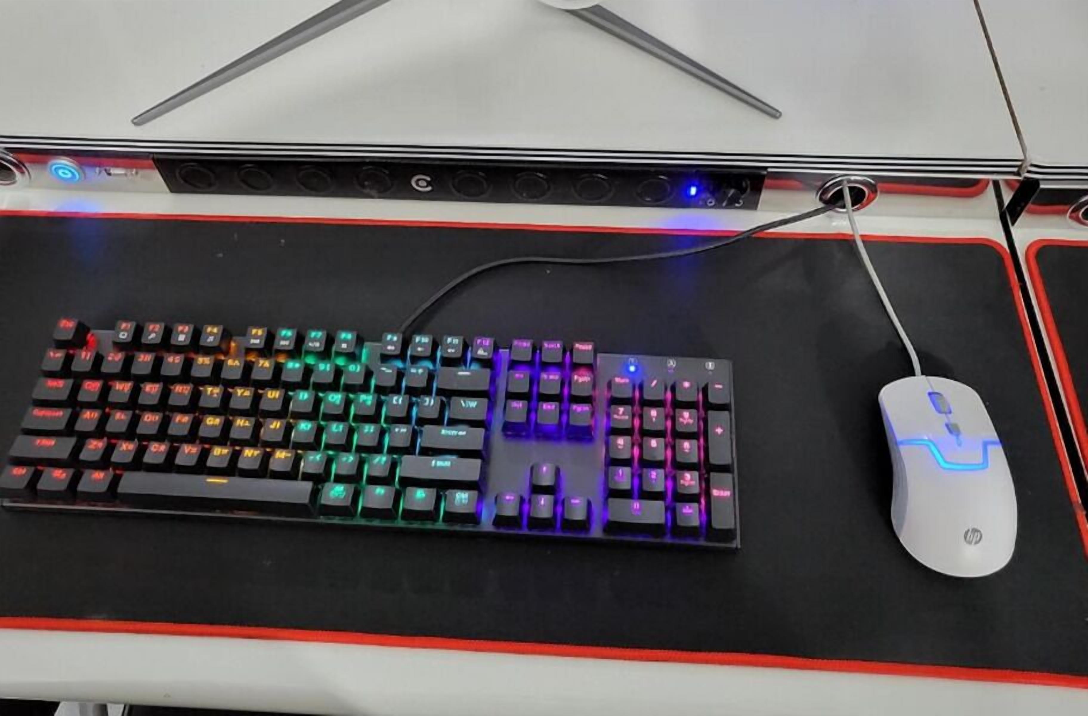A mechanical keyboard with RGB lighting and a wired mouse on a black mouse pad with red accents.