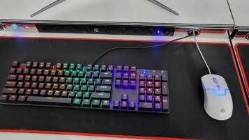 A mechanical keyboard with RGB lighting and a wired mouse on a black mouse pad with red accents.