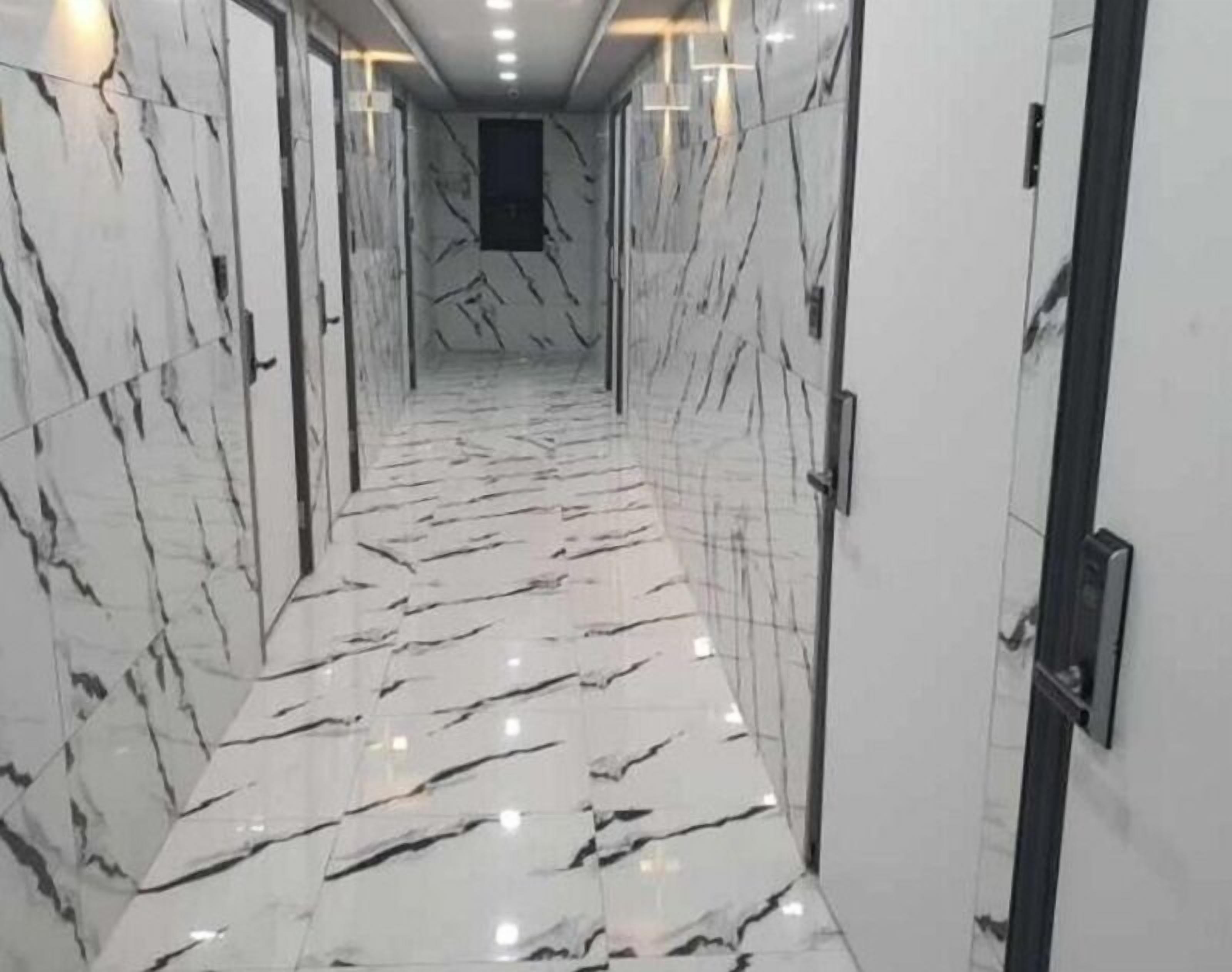 A hallway with marble flooring and walls, leading to a door at the end.