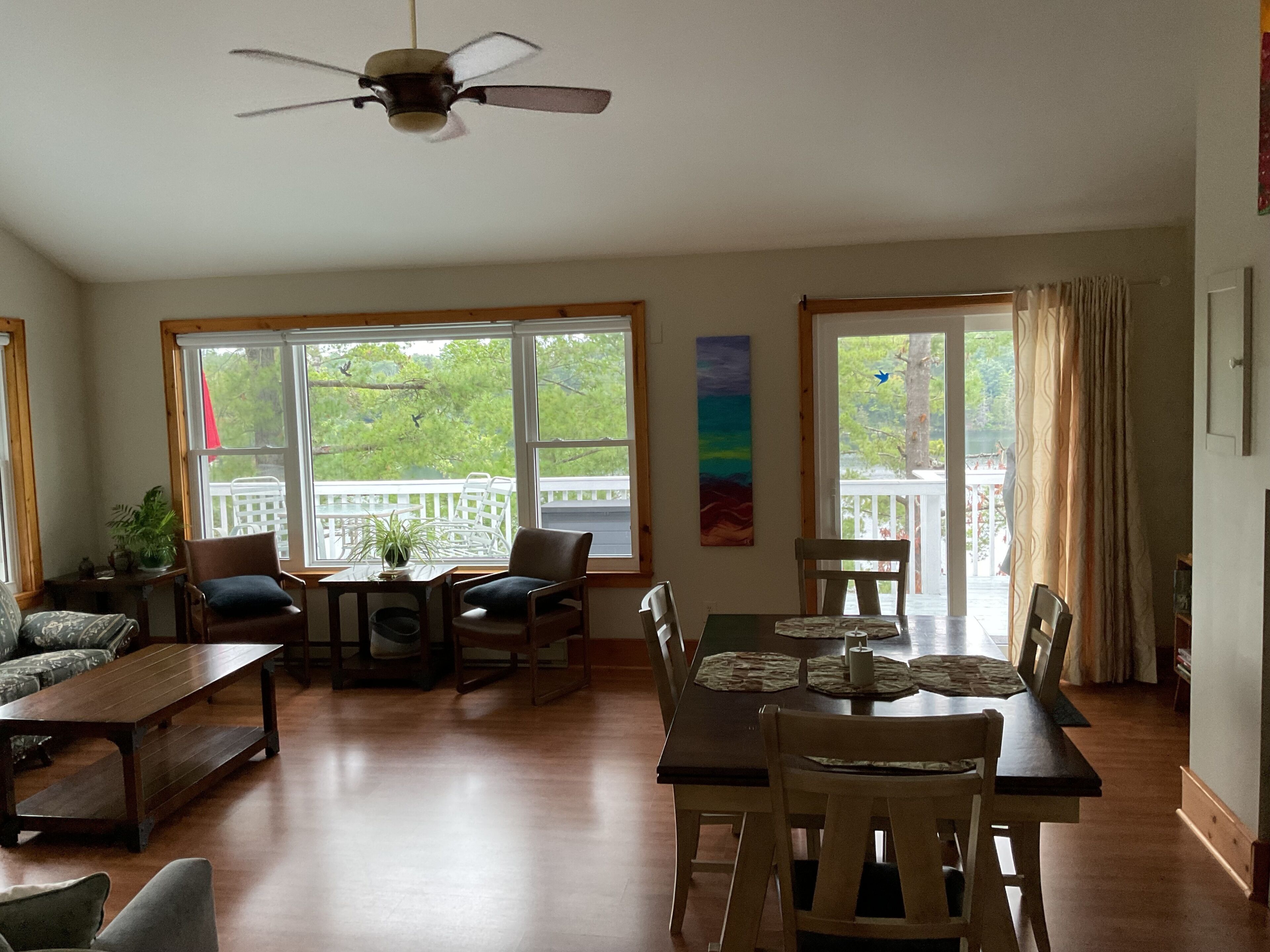 A spacious living room with a dining area, large windows, a ceiling fan, and a view of the outdoors.