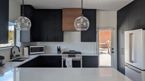 A modern kitchen with black cabinets, a white countertop, a microwave, a stove, and two pendant lights. - Red Wolf Lodge - new detached home - private hot tub - views - EV charger (Fraser)