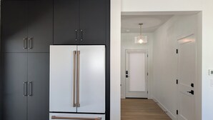 A modern kitchen with a large black and white refrigerator, wooden cabinets, and a wooden floor. - Red Wolf Lodge - new detached home - private hot tub - views - EV charger (Fraser)