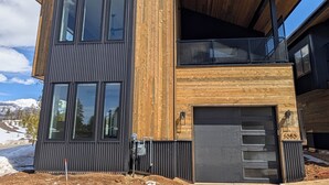A modern two-story house with a combination of dark siding and wooden paneling, large windows, and a visible garage door. - Red Wolf Lodge - new detached home - private hot tub - views - EV charger (Fraser)