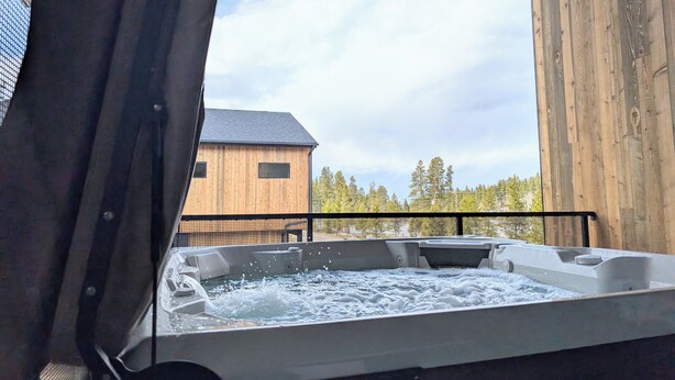 A hot tub with water splashing, a wooden deck, and a building in the background. - Red Wolf Lodge - new detached home - private hot tub - views - EV charger (Fraser)