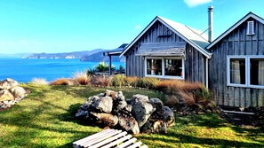A wooden cabin with a view of the ocean, a grassy area with rocks, and a wooden deck.