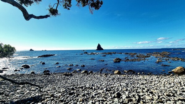 Eine felsige Küstenlinie mit blauem Himmel, einer entfernten Insel und einer markanten Felsformation.