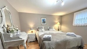 Ein Schlafzimmer mit einem großen Bett, einem Schminktisch, einem Spiegel und einem Fenster mit Spitzenvorhängen.