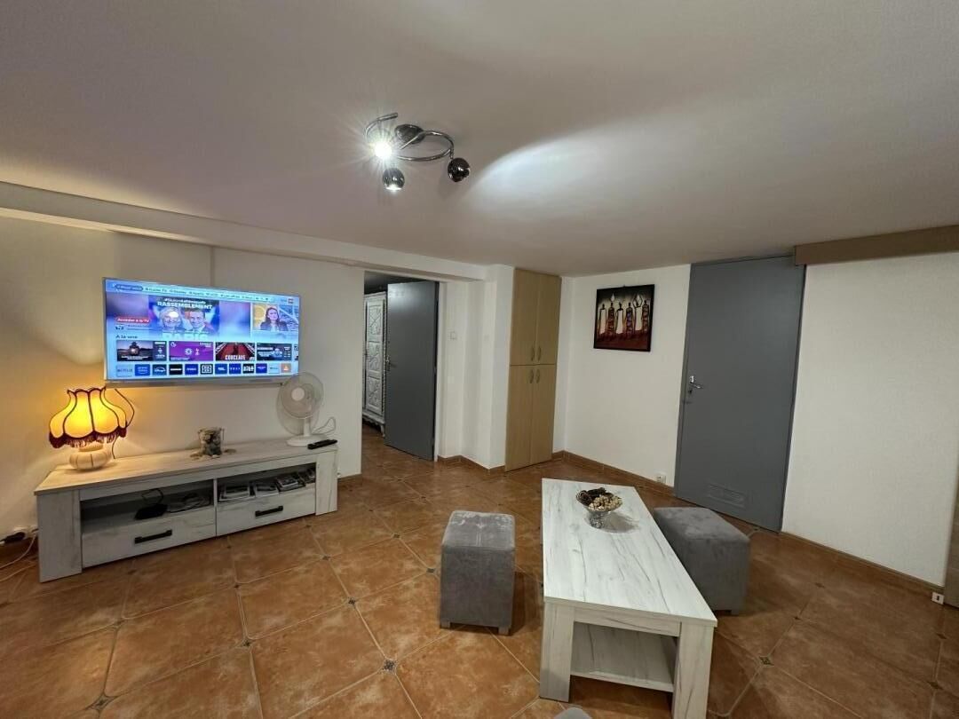 En stue med et fladskærms-TV, en lampe, en ventilator og et lille bord.