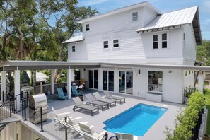 Une maison à deux étages dotée d’un patio couvert comprenant une piscine, des chaises longues et un barbecue.