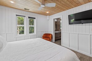 Une chambre à coucher avec un lit, une chaise, un téléviseur fixé au mur et un ventilateur de plafond.