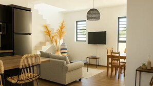 Ein modernes Wohnzimmer mit einer Couch, einem Esstisch und Stühlen. Es gibt eine Küchenzeile mit einem Kühlschrank und einem an der Wand befestigten Fernseher.