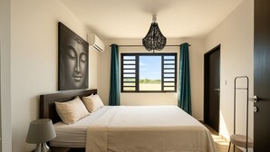 Ein Schlafzimmer mit Bett, Nachttisch, Lampe, Wand-Klimaanlage, einem Fenster mit Vorhängen und einer Tür.