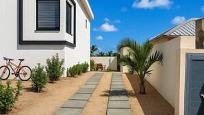 Ein modernes Haus mit Auffahrt, die zum Eingang führt, einem Fahrrad, das vor der Tür steht, und einer Palme im Garten.