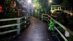 A nighttime pathway with wooden railings, surrounded by greenery and illuminated by street lamps. - Sun Outdoors: Clean, Private, Cozy & Loaded with Perks! Golf Cart Included (Sarasota)