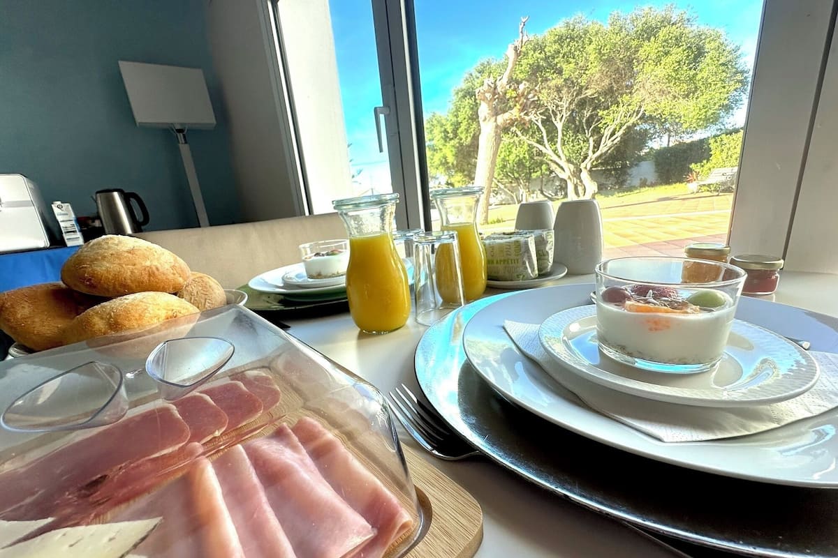 A breakfast setting with croissants, ham, and a glass of orange juice on a table with a view of trees and a building outside.