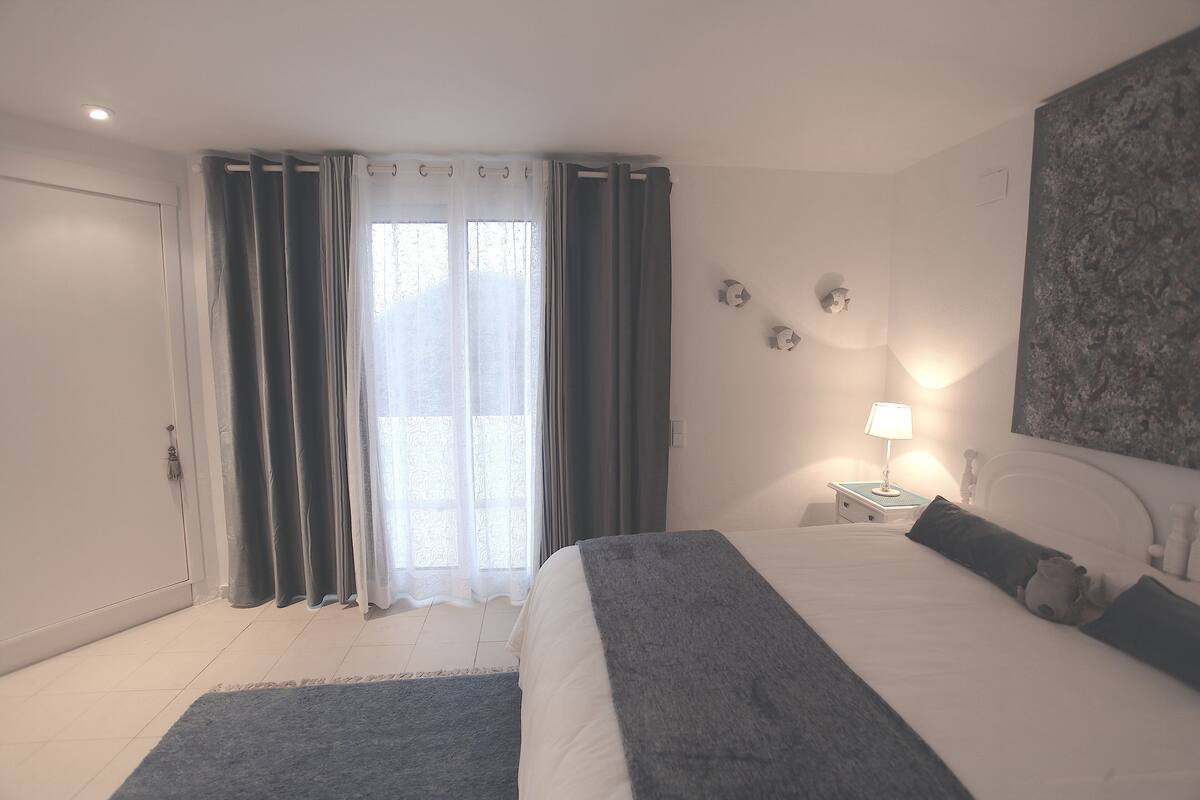 A bedroom with a bed, curtains, a nightstand, a lamp, and a wall art piece.
