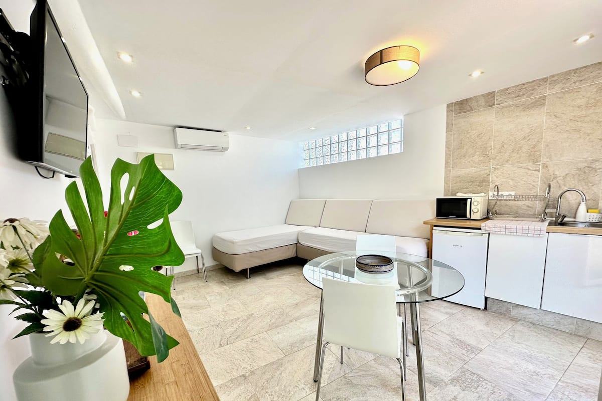 A modern kitchen with a glass dining table, white appliances, and a large window.