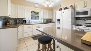A modern kitchen with white cabinets, a large island, a microwave, a refrigerator, and a gas stove. - The American Dream: Historic S Mt Vernon Craftsman (Prescott)