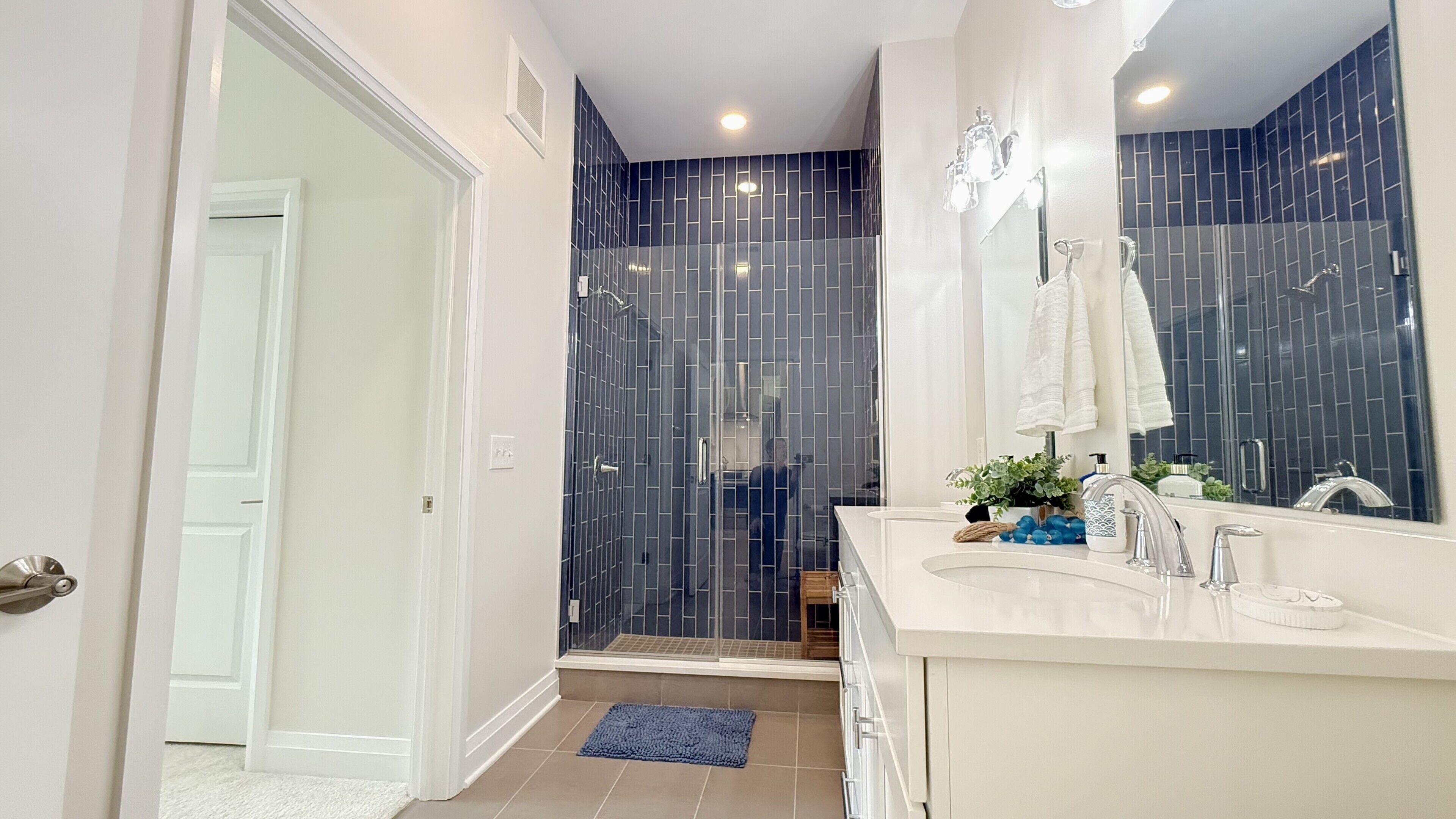 A modern bathroom with a glass shower enclosure, a white vanity with a large mirror, and a blue rug on the floor.