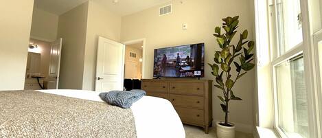 A bedroom with a bed, dresser, television, and a potted plant.