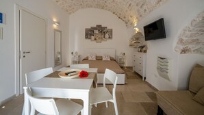 A bedroom with a stone ceiling, a bed with two pillows, a TV, a bedside table, and a small table with a flower. - Velvet Home: charming studio in the heart of center Ostuni (Ostuni)