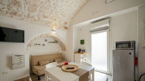 A compact living space with a stone ceiling, a sofa, a dining table, a TV, a kitchen area with a refrigerator, and a sliding door. - Velvet Home: charming studio in the heart of center Ostuni (Ostuni)