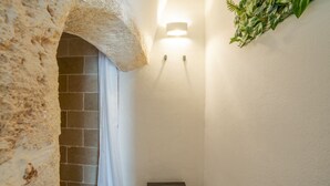 A narrow hallway with a stone archway, a small wooden stool, a wall-mounted light, and a green plant decoration. - Velvet Home: charming studio in the heart of center Ostuni (Ostuni)