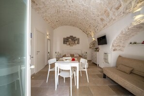 A room with a stone ceiling, a bed, a TV, a sofa, and a dining area with chairs and a table.