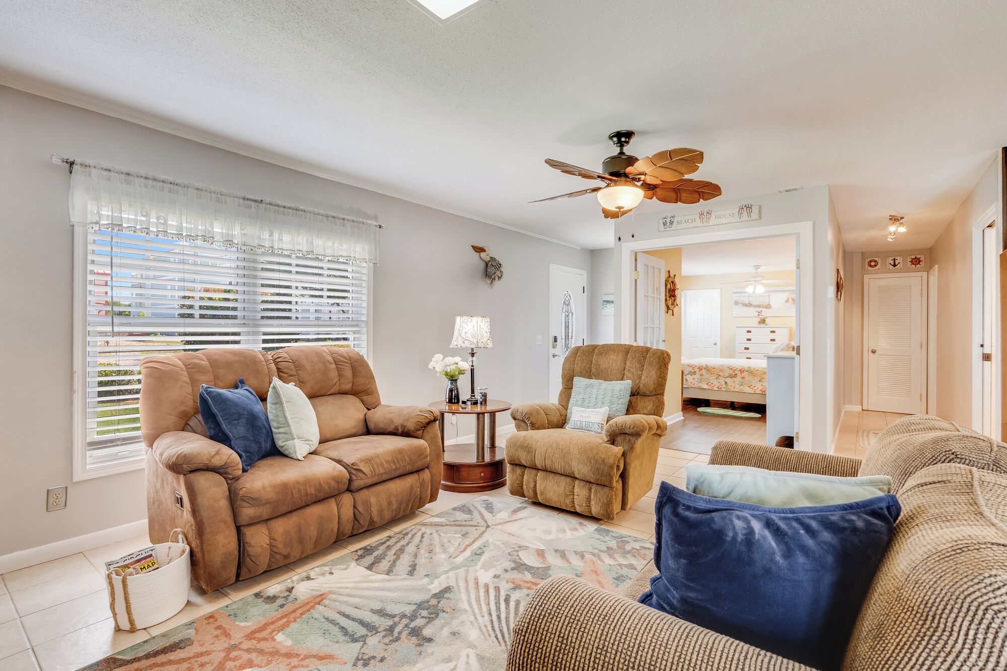 A living room with a brown sofa, a patterned rug, a ceiling fan, and a door leading to a bedroom.