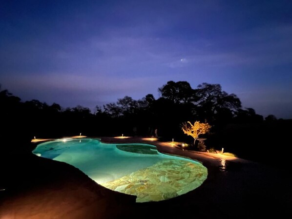 A nighttime swimming pool with illuminated edges and a crescent moon in the sky.