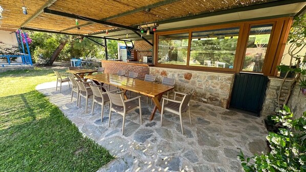 Une terrasse extérieure avec un sol en pierre, une table et des chaises en bois, un mur en briques et une vue sur le jardin.