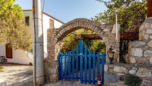 A stone archway leading to a blue gate, with a lamp post and a tree in the background. - Zeytin Pansiyon Palamutbükü (Datca)