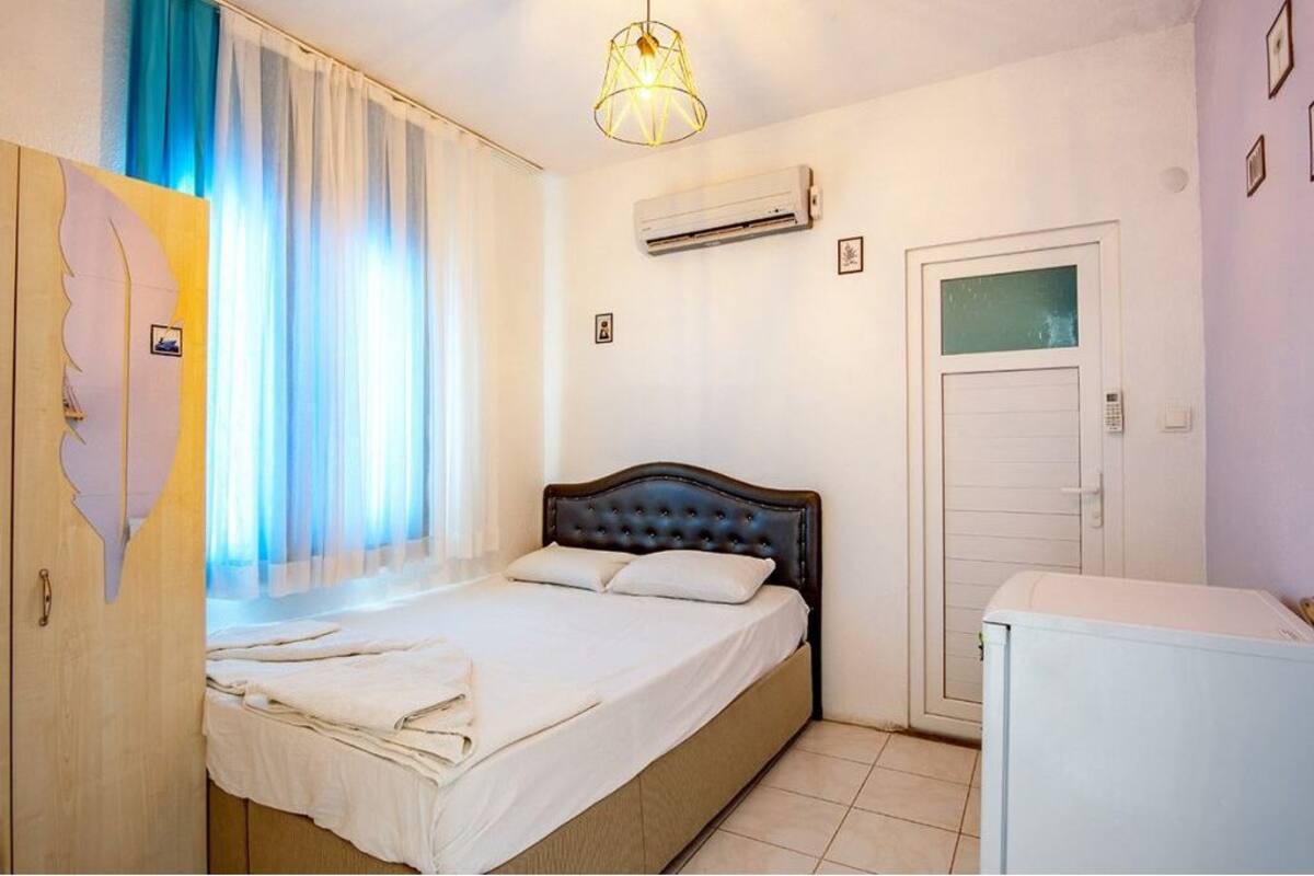 A bedroom with a bed, an air conditioner, a door, and a small white appliance.