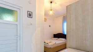 A bedroom with a bed, a bedside table, a hanging light fixture, and a door with frosted glass. - Zeytin Pansiyon Palamutbükü (Datca)