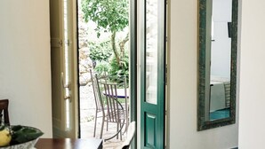 Une porte ouverte donnant sur un espace extérieur avec une table et des chaises, une porte verte et un miroir accroché au mur.