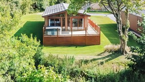 Een houten chalet met terras, omgeven door weelderige begroeiing en een verzorgd gazon.