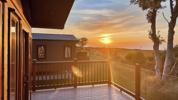 Een houten terras met uitzicht op de zonsondergang, een klein gebouw en een omheind gebied.