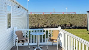 A balcony with two wicker chairs and a small round table, a white railing, and a hedge in the background.