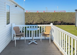Un balcon avec deux fauteuils en osier et une petite table ronde, une balustrade blanche et une haie en arrière-plan.
