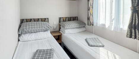 Un dormitorio doble con dos camas individuales, un armario de madera arriba y una ventana con cortinas de estampado de hojas.