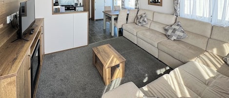 A compact living area with a sofa, a wooden coffee table, a TV, and a kitchenette.