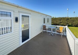 Een stacaravan met een terras, twee stoelen, een tafel en een deur.