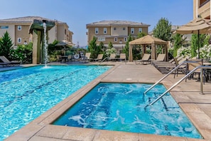 A swimming pool with lounge chairs and umbrellas, surrounded by buildings.