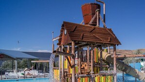 Un parco acquatico con una struttura giochi in legno, una piscina e uno scivolo d'acqua gigante.